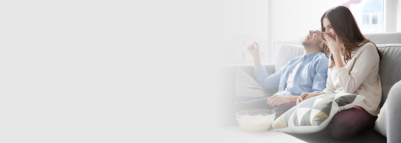 Çift që qesh ndërsa janë ulur në divan me kokoshka.