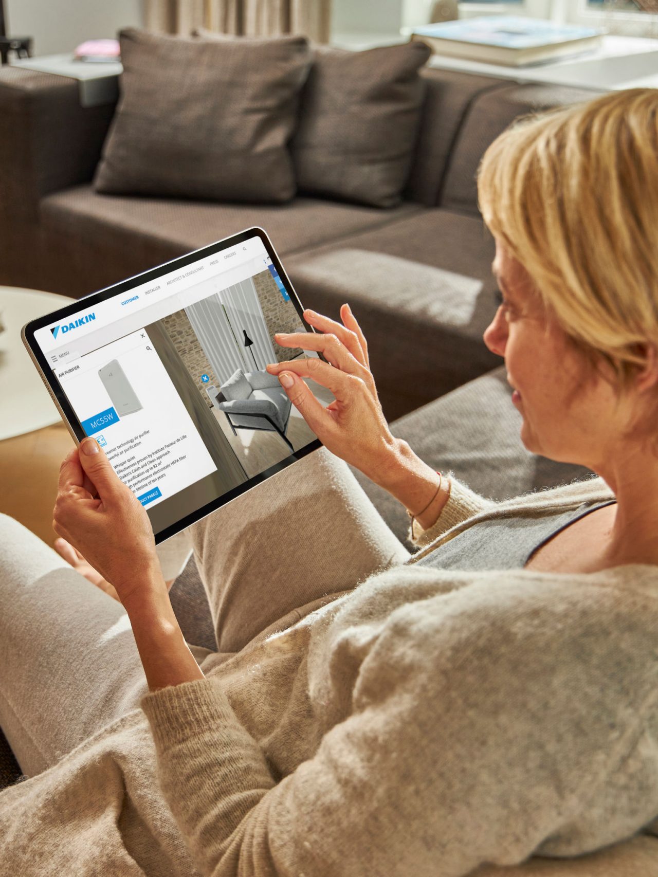 Një grua e ulur në një divan duke parë kondicionerët në qendrën e përvojës virtuale në tablet